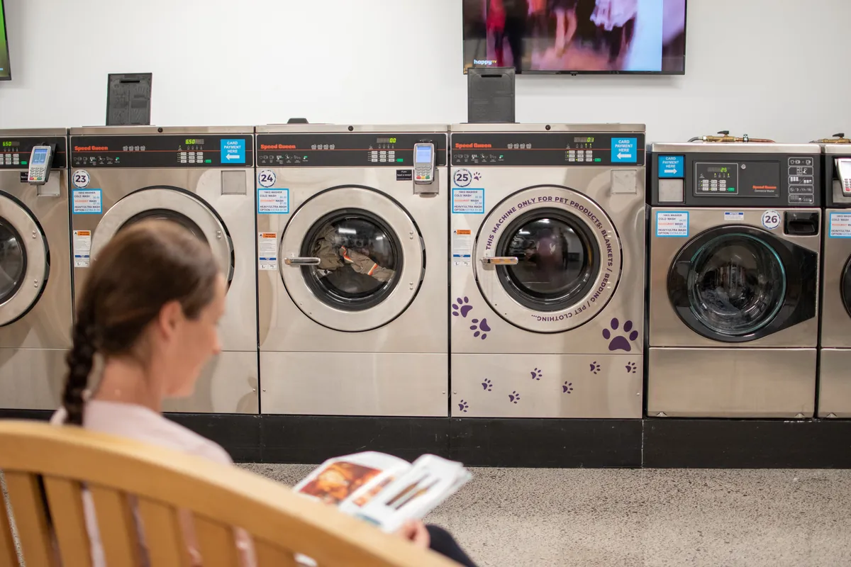 Customer relaxing with a magazine while washing runs at Coast Laundromat near Gulf Harbour